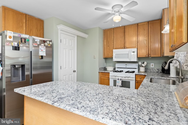 kitchen with light stone countertops, white appliances, a sink, a ceiling fan, and brown cabinets