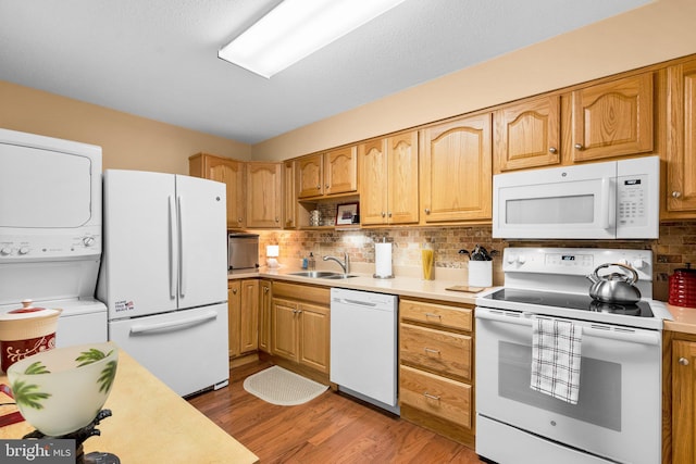 kitchen with sink, white appliances, stacked washing maching and dryer, hardwood / wood-style floors, and decorative backsplash