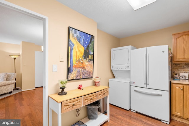 laundry area featuring stacked washer / drying machine and light hardwood / wood-style flooring