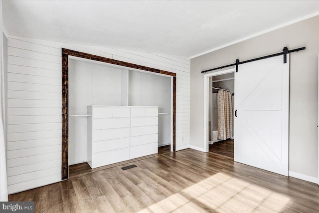 unfurnished bedroom featuring a barn door, a closet, wood finished floors, and visible vents