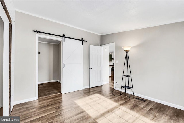 unfurnished bedroom featuring a barn door, wood finished floors, visible vents, baseboards, and ornamental molding