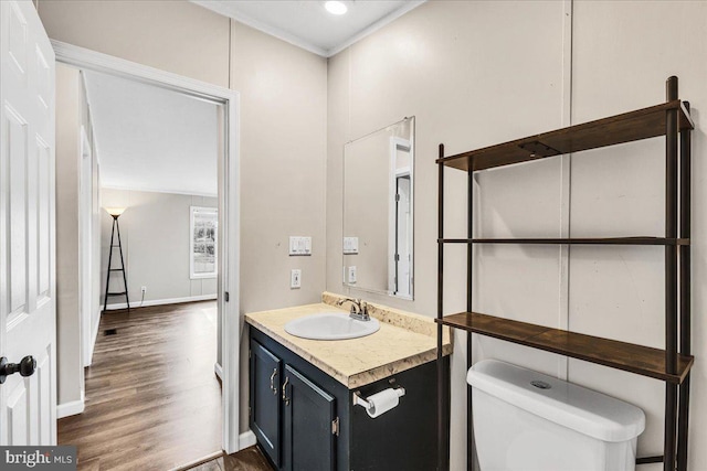 half bath with baseboards, toilet, ornamental molding, wood finished floors, and vanity