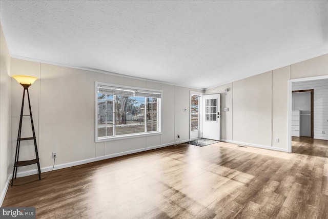 unfurnished living room with a textured ceiling, wood finished floors, and baseboards