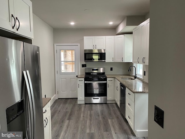 kitchen featuring sink, white cabinetry, hardwood / wood-style floors, stainless steel appliances, and light stone countertops