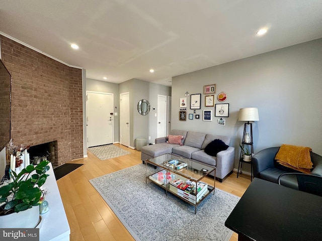 living room with light wood-style flooring, recessed lighting, brick wall, a fireplace, and baseboards