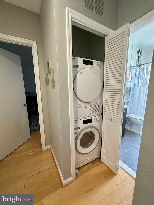 washroom featuring stacked washer / dryer, laundry area, light wood-type flooring, and visible vents