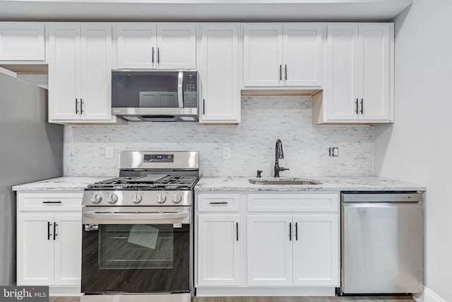 kitchen with a sink, appliances with stainless steel finishes, light stone countertops, and white cabinetry