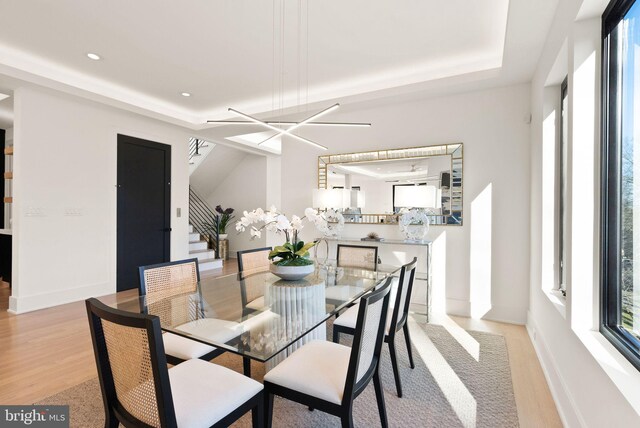 dining space featuring a raised ceiling, an inviting chandelier, and light hardwood / wood-style flooring