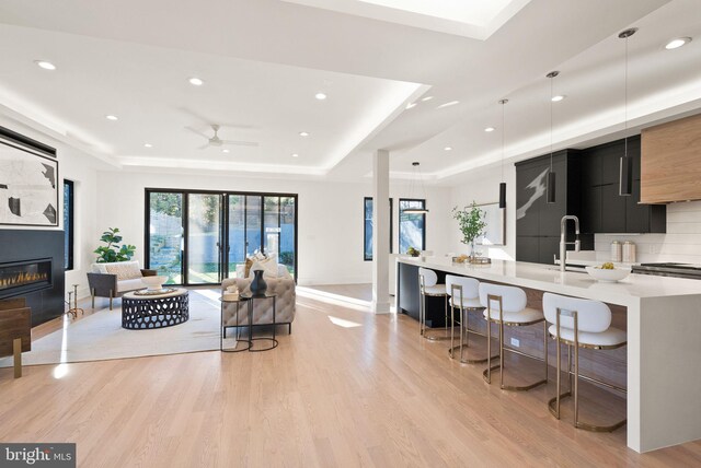 living room featuring sink, a raised ceiling, ceiling fan, and light wood-type flooring