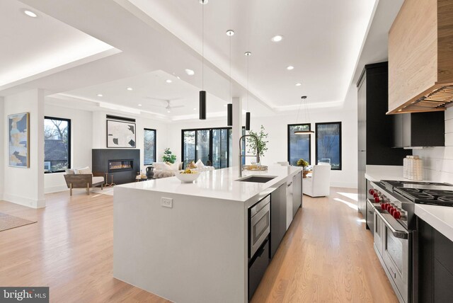 kitchen featuring a raised ceiling, a kitchen island with sink, stainless steel appliances, and decorative light fixtures