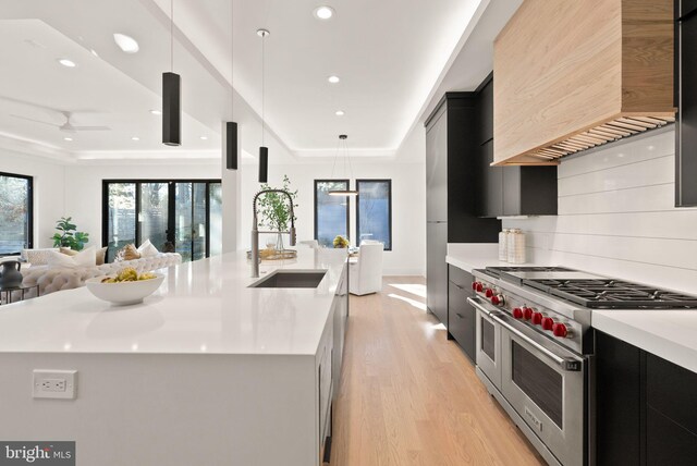 kitchen featuring sink, hanging light fixtures, a center island with sink, double oven range, and a raised ceiling