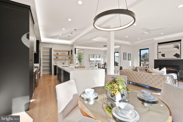 dining area featuring sink, light wood-type flooring, and a tray ceiling