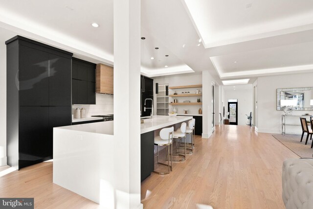 kitchen with a large island, light hardwood / wood-style flooring, backsplash, a kitchen bar, and a raised ceiling