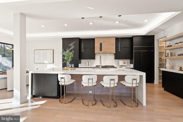 kitchen with light hardwood / wood-style flooring, paneled built in refrigerator, a kitchen breakfast bar, pendant lighting, and a kitchen island with sink