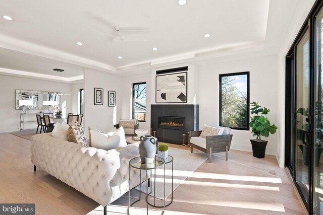 living room featuring a tray ceiling, light hardwood / wood-style floors, and a tile fireplace