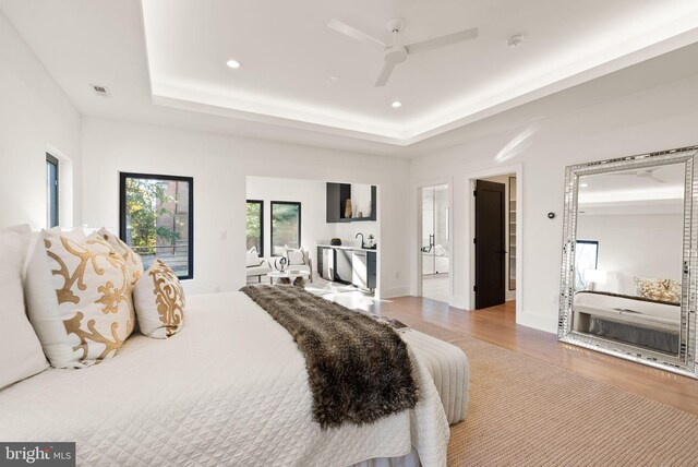 bedroom with a raised ceiling, ceiling fan, and light hardwood / wood-style floors