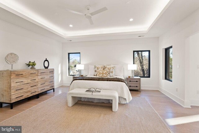 bedroom with wood-type flooring, a raised ceiling, and ceiling fan