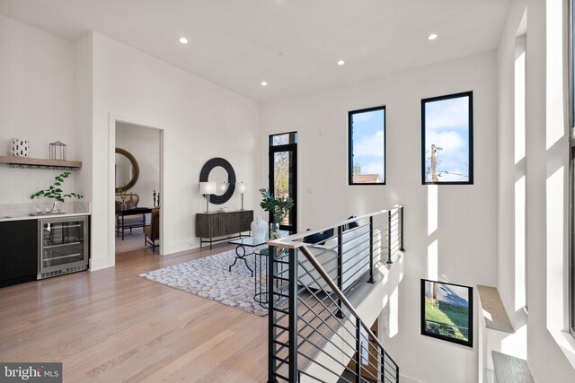 hall with light hardwood / wood-style flooring, beverage cooler, and a high ceiling