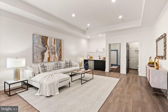 living room with wet bar, a raised ceiling, and hardwood / wood-style floors