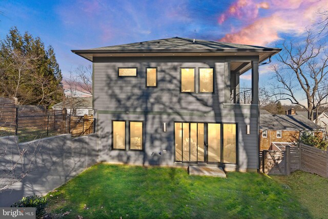 back house at dusk featuring a balcony and a yard