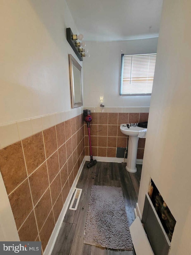 bathroom with a sink, visible vents, wood finished floors, tile walls, and wainscoting