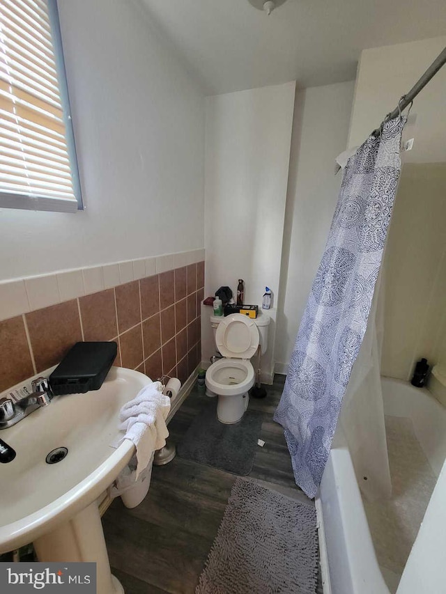 bathroom featuring toilet, shower / tub combo, a sink, wood finished floors, and tile walls