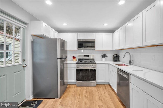 kitchen with sink, light hardwood / wood-style flooring, stainless steel appliances, tasteful backsplash, and white cabinets