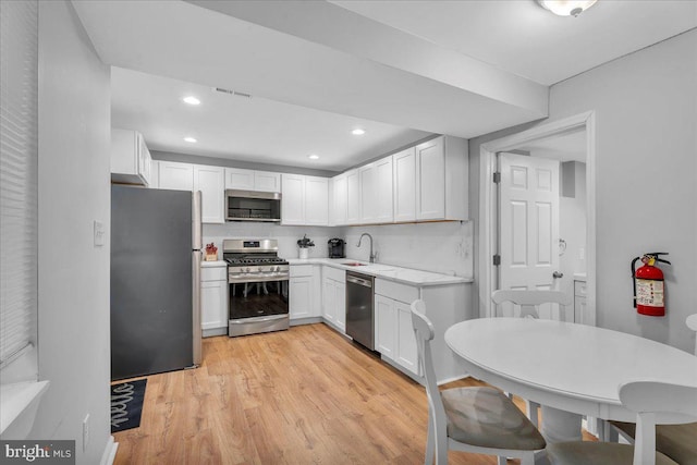 kitchen featuring tasteful backsplash, white cabinetry, sink, stainless steel appliances, and light hardwood / wood-style flooring