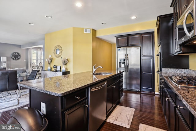 kitchen with sink, stone counters, appliances with stainless steel finishes, a center island with sink, and dark hardwood / wood-style flooring