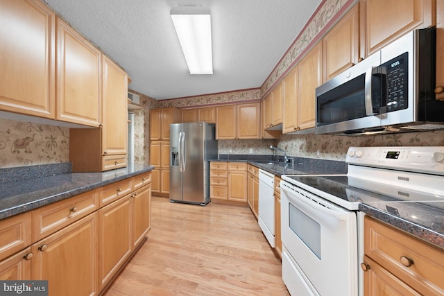 kitchen with sink, dark stone counters, stainless steel appliances, a textured ceiling, and light hardwood / wood-style flooring