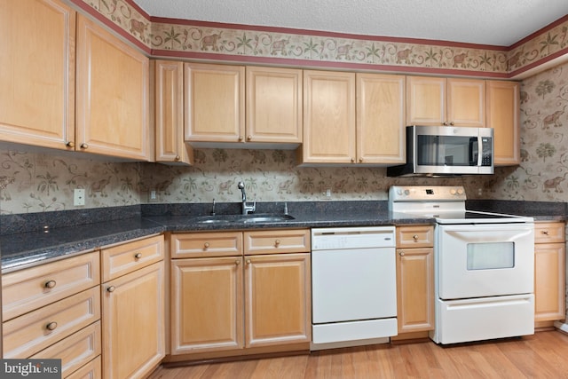 kitchen featuring sink, light hardwood / wood-style flooring, a textured ceiling, white appliances, and dark stone counters