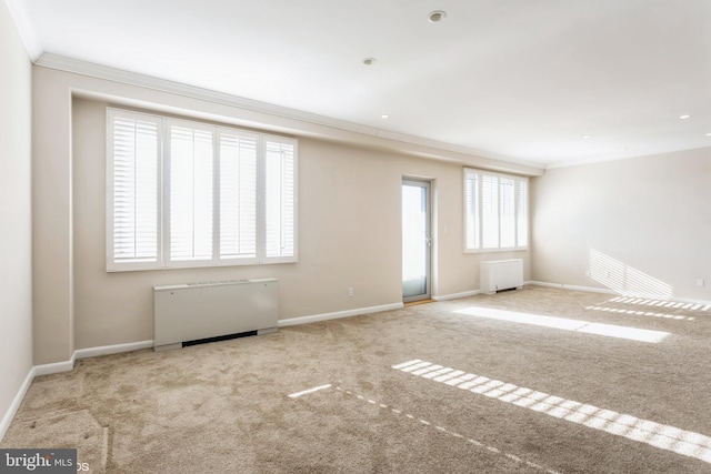 empty room featuring crown molding, radiator heating unit, and light colored carpet