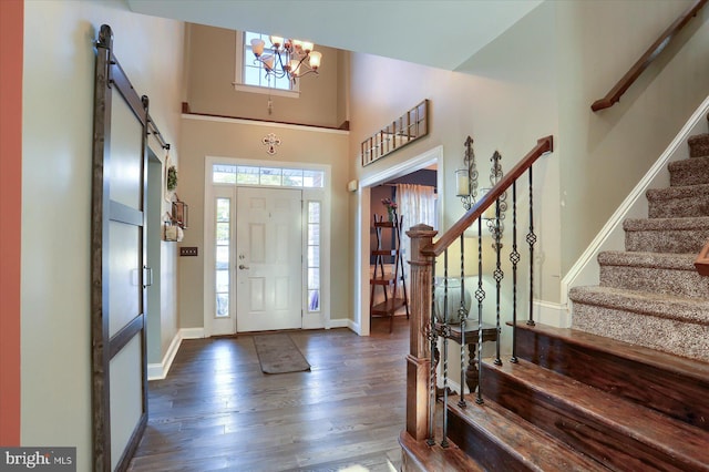 foyer with dark hardwood / wood-style flooring, a barn door, a chandelier, and a high ceiling