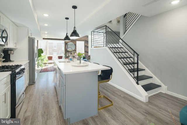 kitchen with a center island with sink, a sink, stainless steel appliances, light countertops, and light wood-style floors