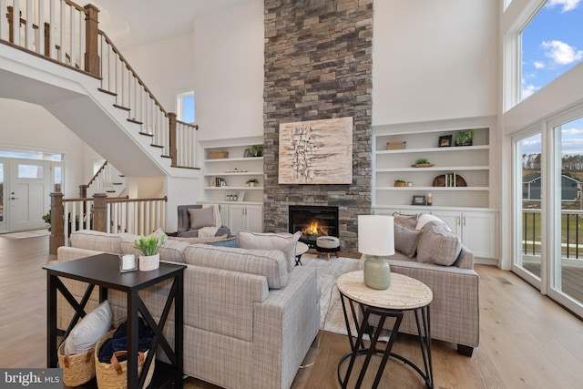 living room featuring a high ceiling, a stone fireplace, light hardwood / wood-style floors, and built in shelves