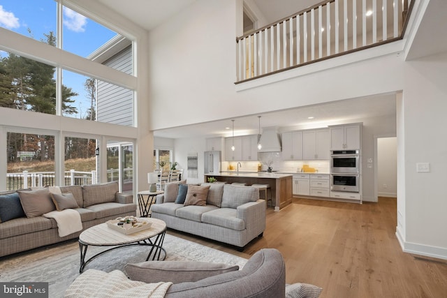 living room featuring a towering ceiling, a healthy amount of sunlight, sink, and light hardwood / wood-style flooring