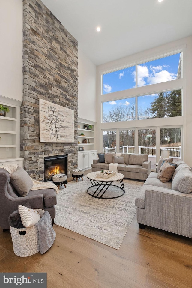 living room featuring a towering ceiling, wood-type flooring, a fireplace, and built in features