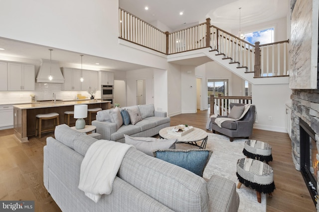 living room with wood-type flooring, a stone fireplace, sink, and a towering ceiling