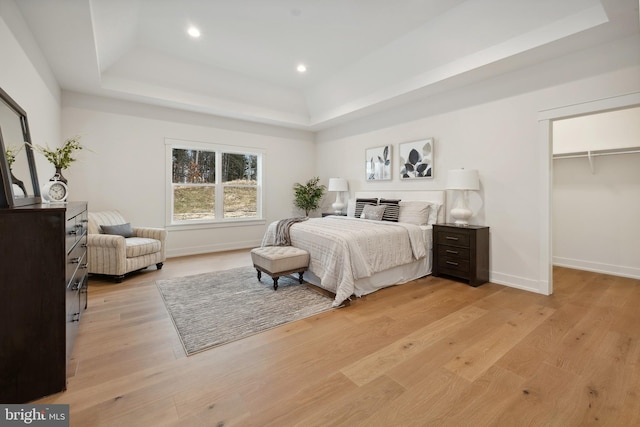 bedroom with a raised ceiling, a walk in closet, and light hardwood / wood-style flooring