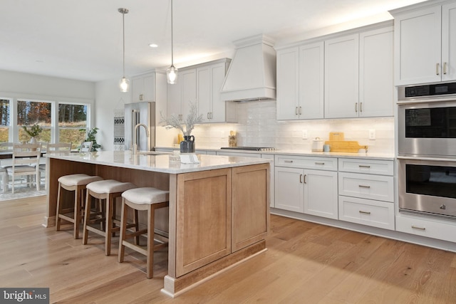 kitchen featuring decorative light fixtures, an island with sink, white cabinets, and premium range hood