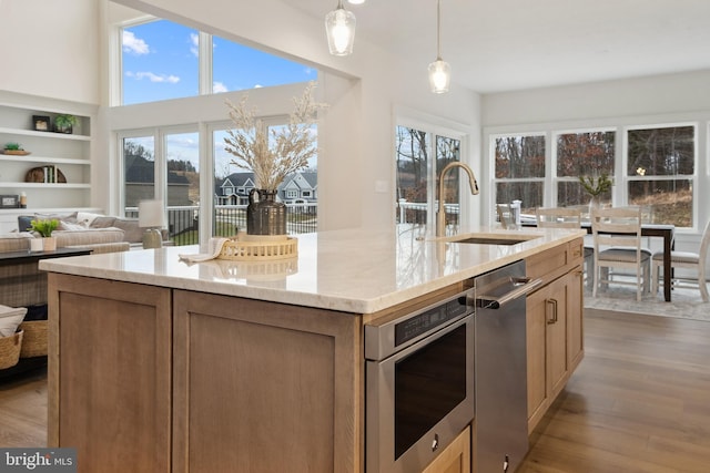 kitchen with an island with sink, sink, hanging light fixtures, light hardwood / wood-style floors, and a healthy amount of sunlight