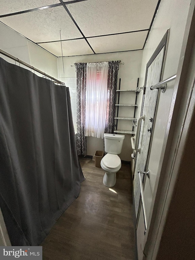 bathroom featuring a shower with shower curtain, a drop ceiling, toilet, and wood finished floors