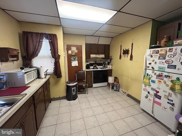 kitchen with a paneled ceiling, dark brown cabinets, range with gas stovetop, light tile patterned flooring, and white fridge