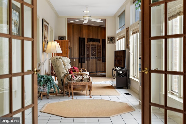 interior space featuring light tile patterned floors, crown molding, ceiling fan, and wood walls