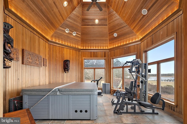 exercise room featuring a hot tub, a water view, wooden walls, and high vaulted ceiling