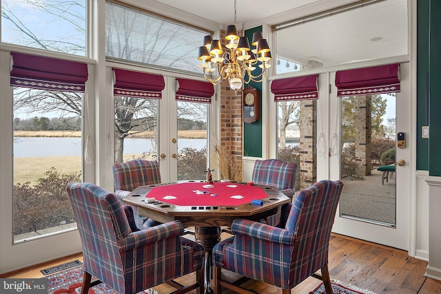 dining space featuring hardwood / wood-style flooring, a water view, a chandelier, and french doors