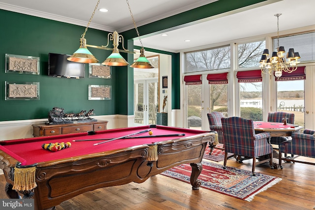 recreation room featuring wood-type flooring, crown molding, a water view, an inviting chandelier, and french doors