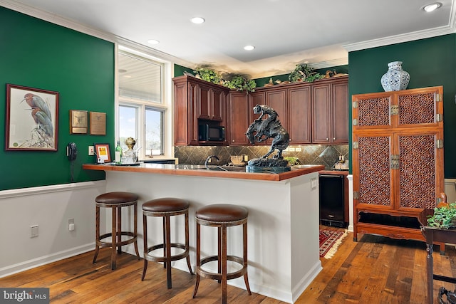 kitchen with dark hardwood / wood-style floors, black appliances, kitchen peninsula, and a breakfast bar