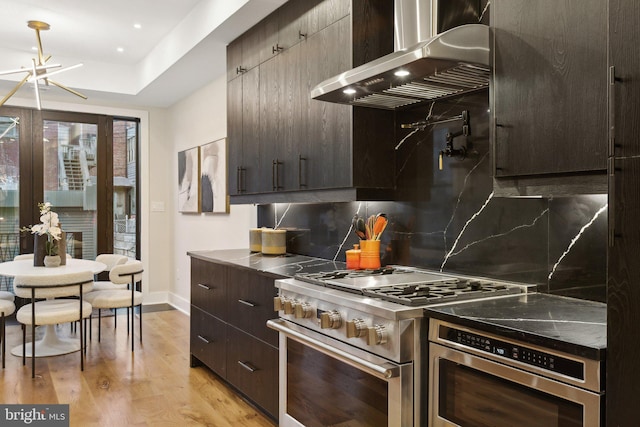 kitchen featuring wall chimney exhaust hood, tasteful backsplash, dark brown cabinets, light wood-type flooring, and stainless steel stove