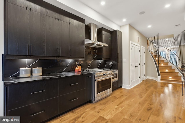 kitchen with high end stainless steel range oven, tasteful backsplash, light hardwood / wood-style flooring, and wall chimney range hood